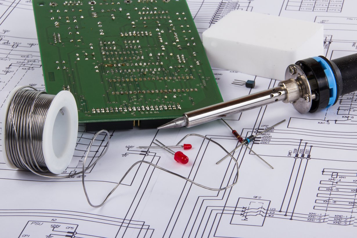 Symbolbild für die Instandsetzung eines Messgeräts mit Lötkolben, Platine, Zubehör und Schaltplan.