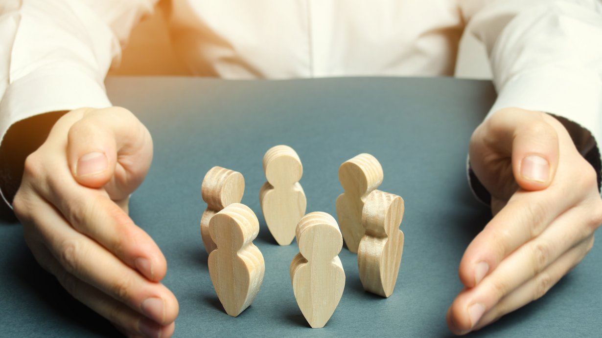 Zwei Hände legen sich schützend um Holzfiguren herum