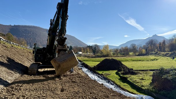 Ein Bagger auf einer Erdpiste neben einer Straße.