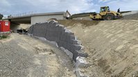 Das Bild zeigt eine Stützwand. Auf der Böschung steht eine Walze, die den Boden verdichtet. Der Hang wird gerade noch aufgeschüttet. Im Vordergrund ist schon zu erkennen, dass der Radweg parallel zu der Stützwand verlaufen wird. 