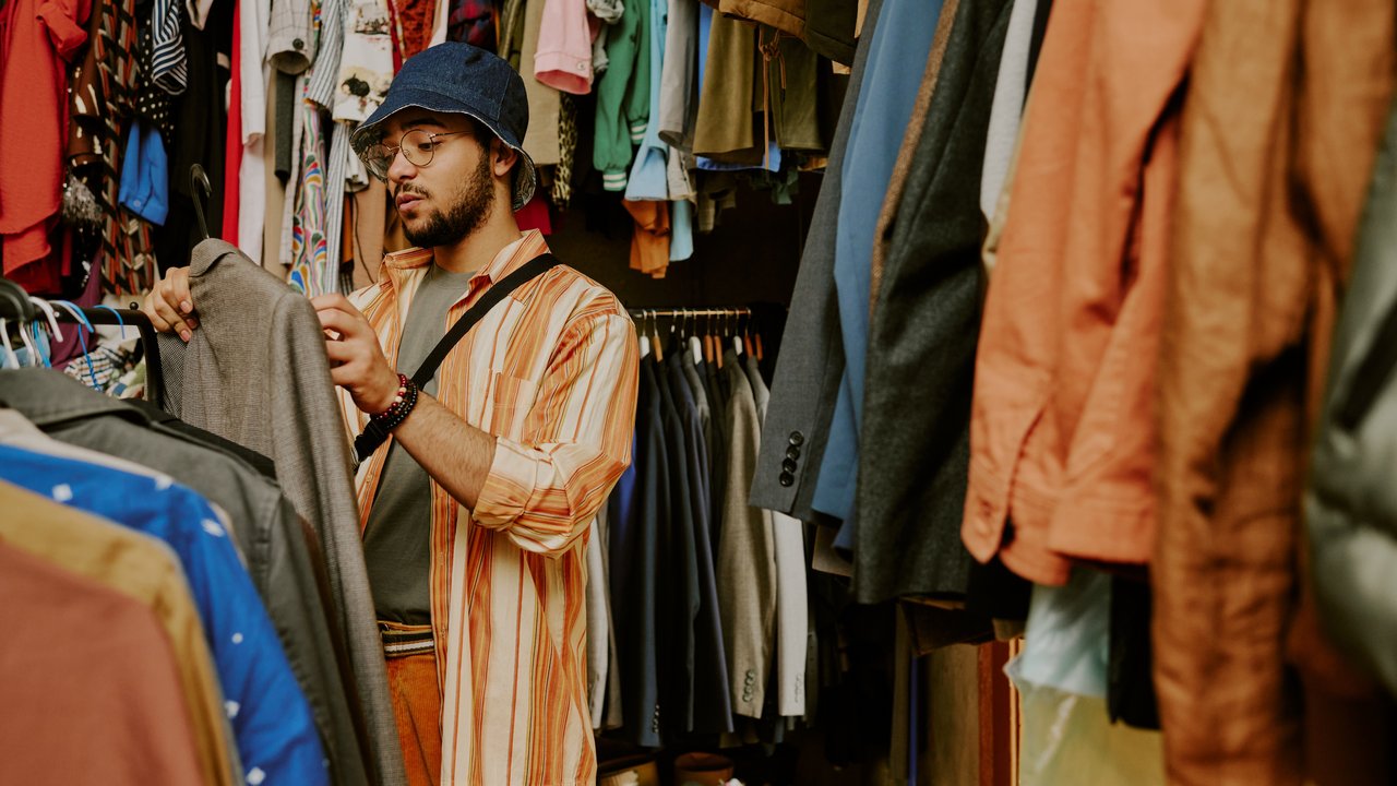 Ein junger Mann steht zwischen Kleiderständern und blickt auf das Kleidungsetikett