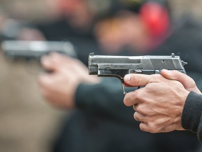 Sportschützen, die Schützen sieht man nur im Hintergrund, im Vordergrund ist eine Pistole, die abgefeuert wird