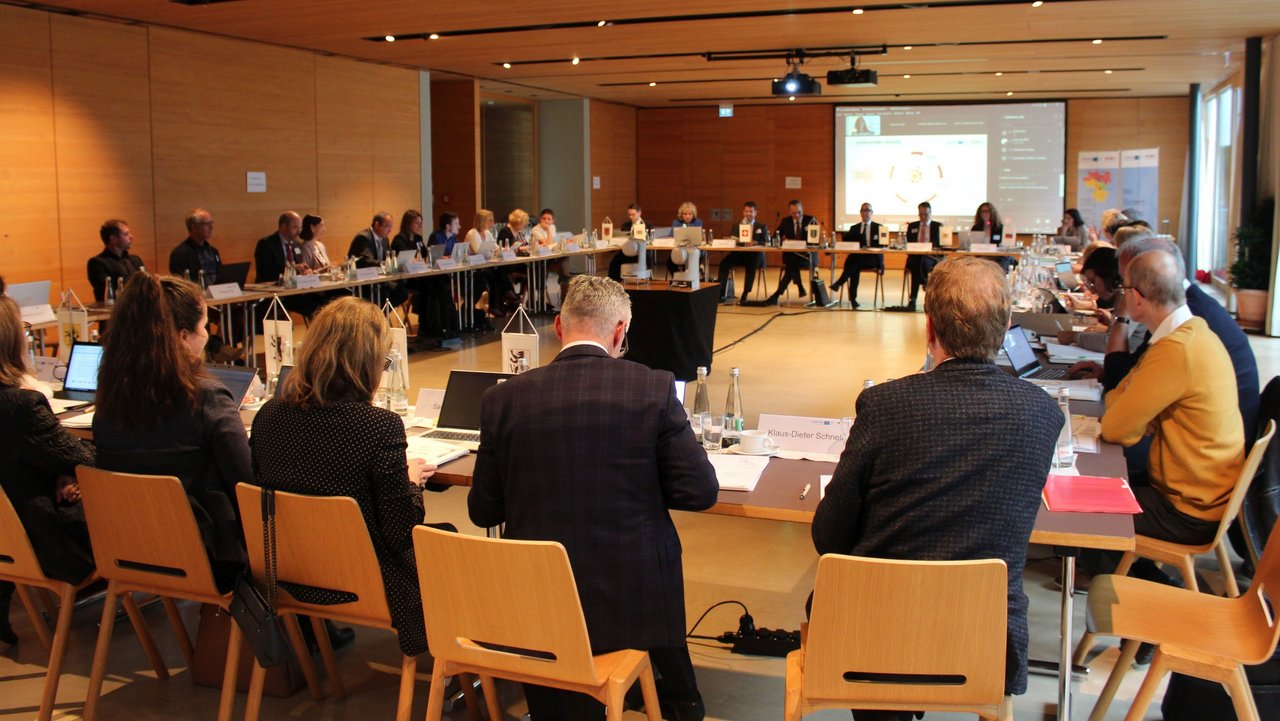 Das Bild zeigt die Teilnehmer der Konstituierenden Sitzung des Interreg-Begleitausschusses in einem Sitzungssaal an Tischen