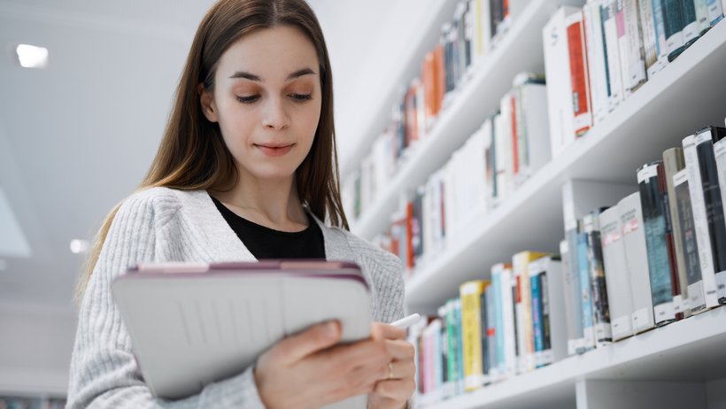 eine junge Frau steht vor dem Regal und blickt in Unterlagen