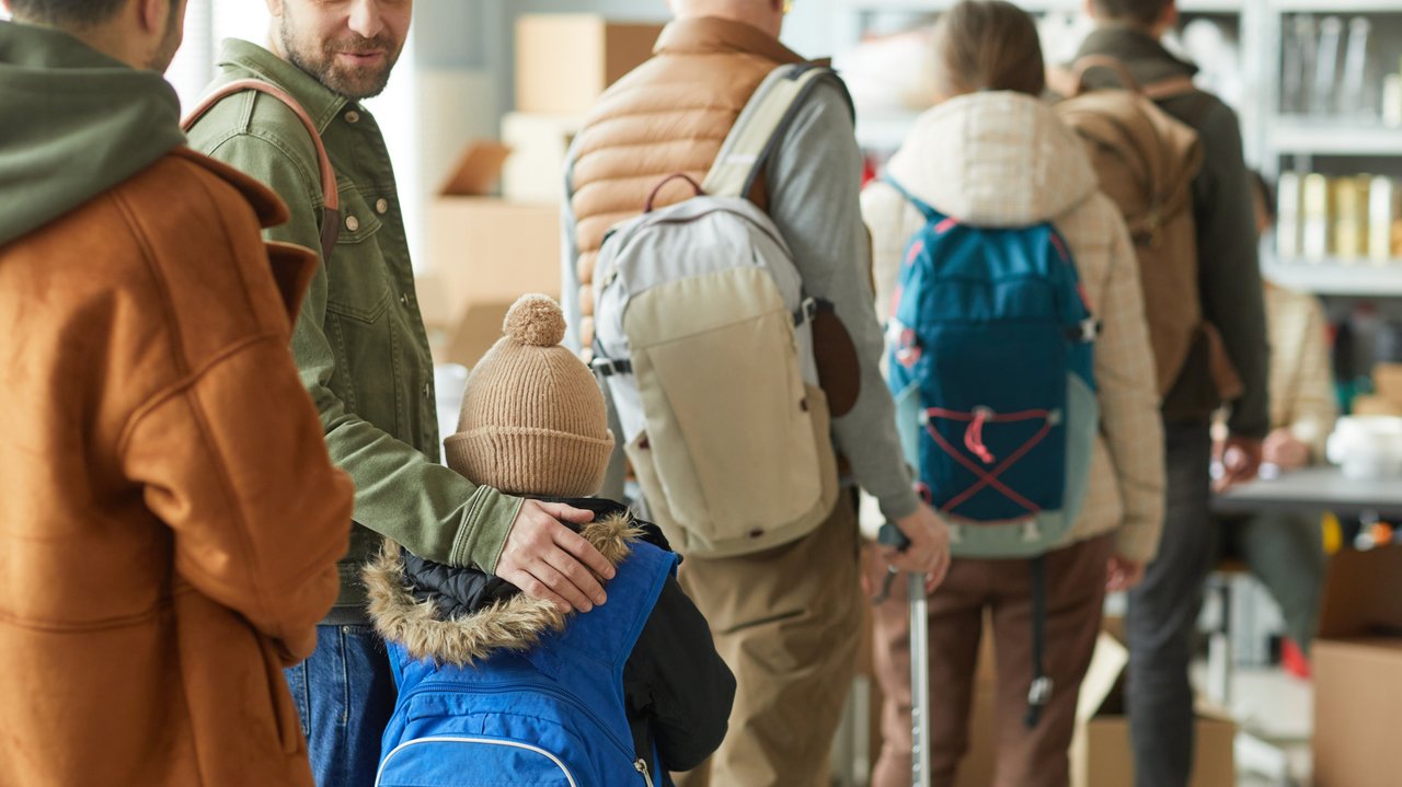 Rückansicht einer Gruppe Flüchtlinge in der Schlange, Fokus auf kleines Kind mit Rucksack