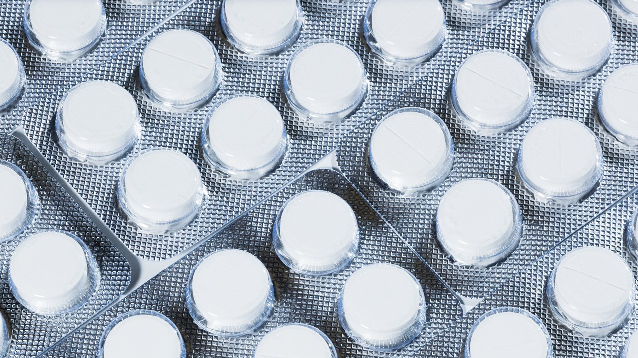 Das Bild zeigt weiße Tabletten in einer Sichtverpackung mit silbernem Hintergrund