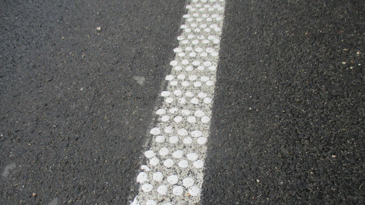 Das Bild zeigt einen Ausschnitt eine Fahrbahnbelags mit weißer Markierung