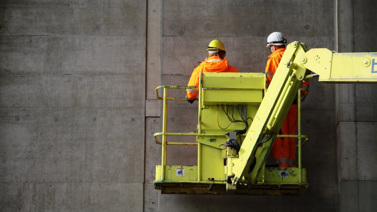 Das Foto zeigt die Prüfung einem Bauwerk mit einer Hubarbeitsbühne. Zwei Männer stehen darin.