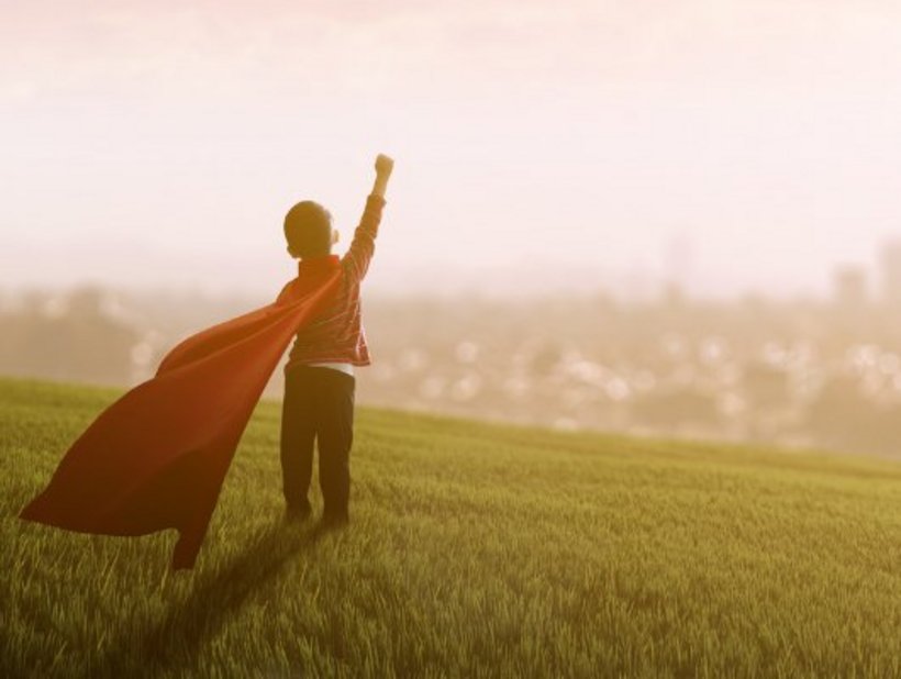 ein kleiner Junge spielt einen Helden und streckt die Faust in die Luft