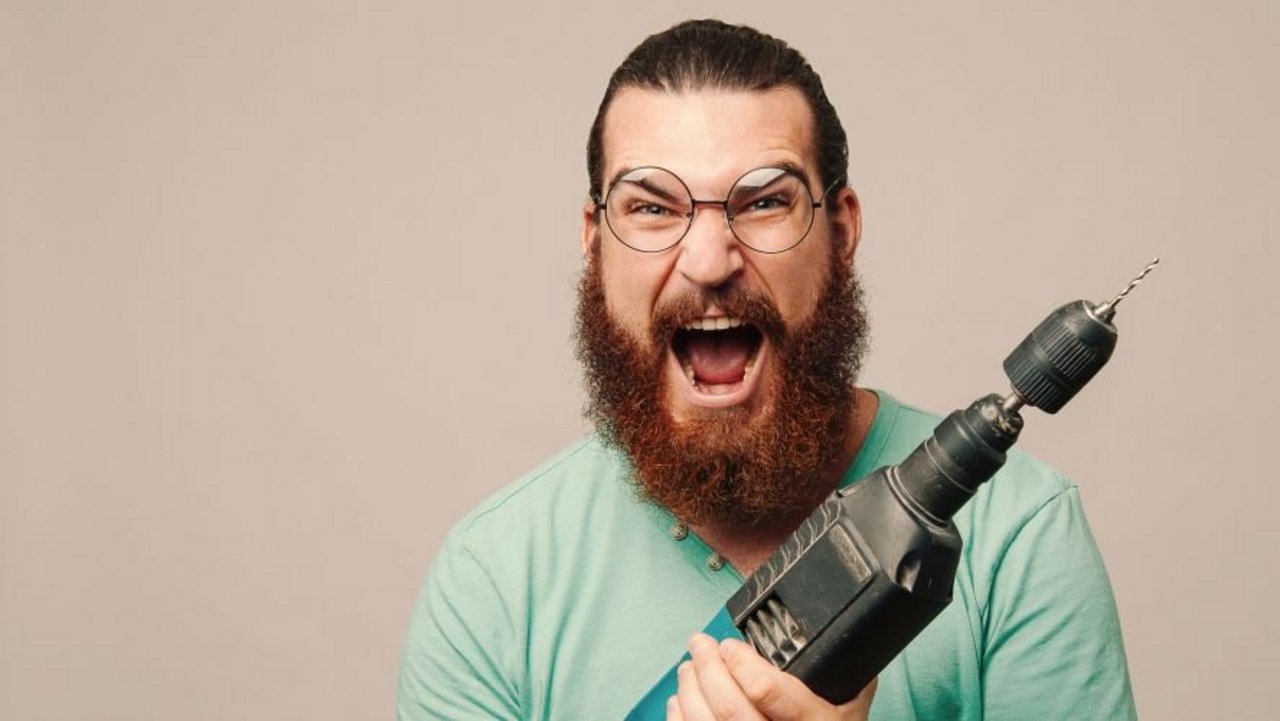 Junger Mann mit einem breiten Grinsen hält eine Schlagbohrmaschine in der Hand