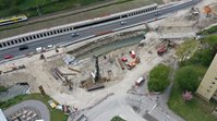 Luftbild einer Baustelle, auf der zwei Brücken abgerissen wurden. Die Straßen enden an den Böschungen des Flusses, dazwischen liegen Rohre zur Wasserhaltung und Baumaschinen arbeiten.
