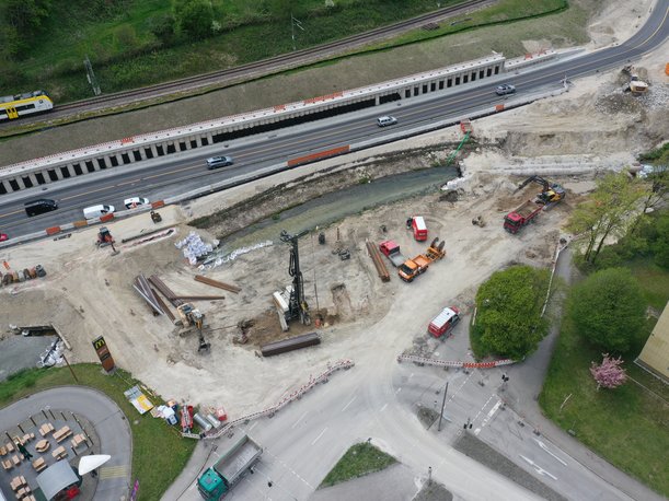Luftbild einer Baustelle, auf der zwei Brücken abgerissen wurden. Die Straßen enden an den Böschungen des Flusses, dazwischen liegen Rohre zur Wasserhaltung und Baumaschinen arbeiten.