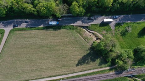 Luftbild Luftbild einer Straße neben einem Feld. Die Straße überbrückt einen kleinen Bach mit einer kurzen Brücke.