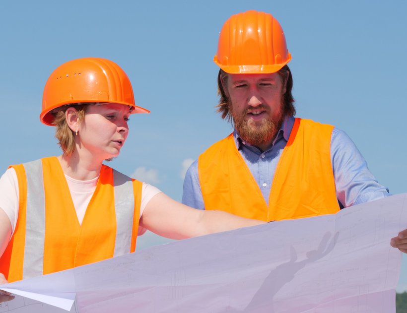 Eine Referendarin und ein Referendar im Straßenbau schauen sich einen Plan an und sprechen darüber. 