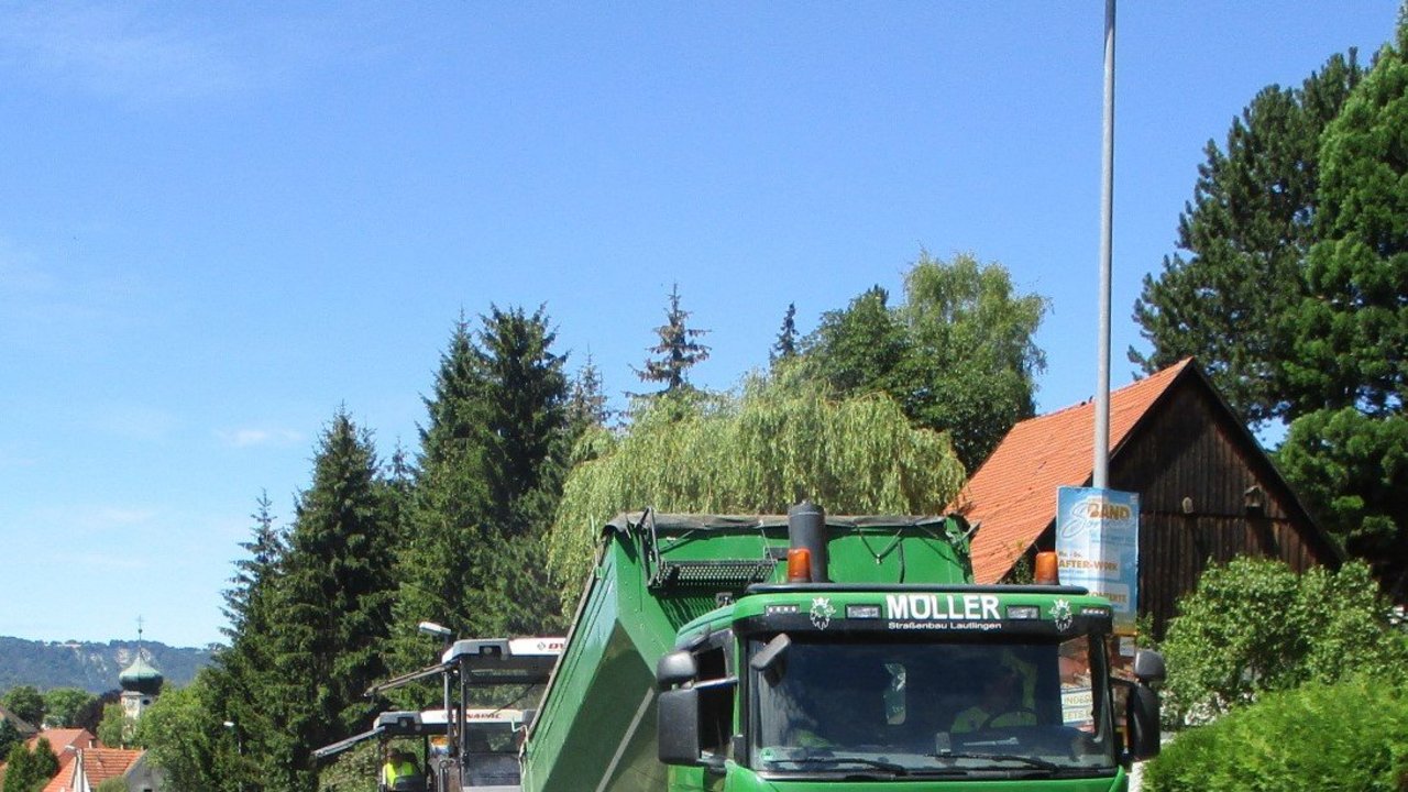 Ein grüner Lastwagen schüttet Asphalt in einen Aufbereiter
