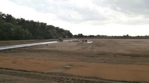 Einbau der Dichtungsschicht (Sandunterlage und Bentonitmatten) mit einem Asphaltfertiger