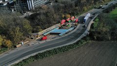 Ein Luftbild einer Baustelle. Über einem graben ist eine H-förmige Betonkonstruktion zu sehen. Neben der Baustelle verläuft eine Behelfsumfahrung.