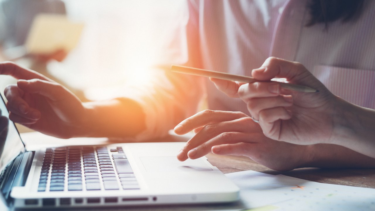 Frau sitzt am PC und arbeitet, im Hintergrund scheint die Sonne