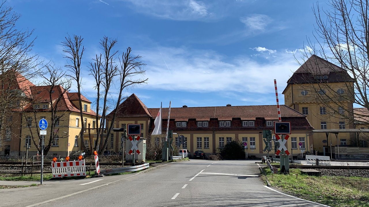 Man blickt auf einen Bahnübergang mit geöffneten Schranken; dahinter sieht man das Bahnbetriebswerk in Tübingen