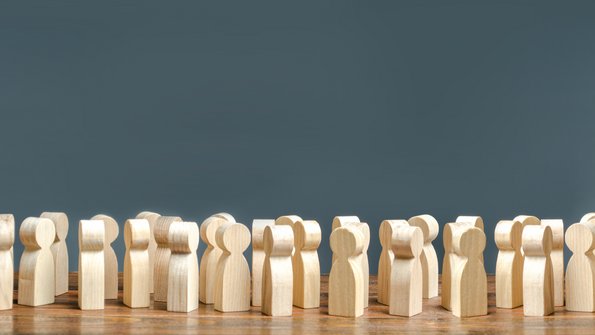 Viele Holzfigürchen sthen vor einem grauen Hintergrund und sind sich so zugewandt, als ob sie miteinander sprechen würden