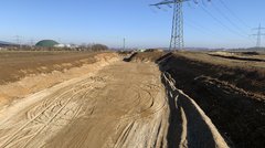 Ein langer Erdeinschnitt, im Hintergrund ein Strommast.