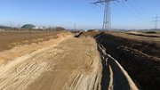 Ein langer Erdeinschnitt, im Hintergrund ein Strommast.