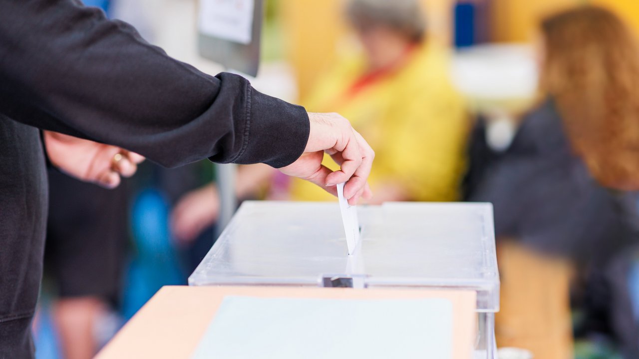 Das Foto zeigt eine Person, die einen Umschlag in eine Wahlurne steckt