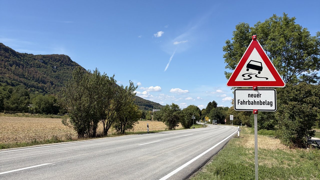 Das Foto zeigt die B 28 zwischen Bad Urach und Dettingen a. d. E.. An der Seite ein Schild mit der Aufschrift "Neuer Fahrbahnbelag"