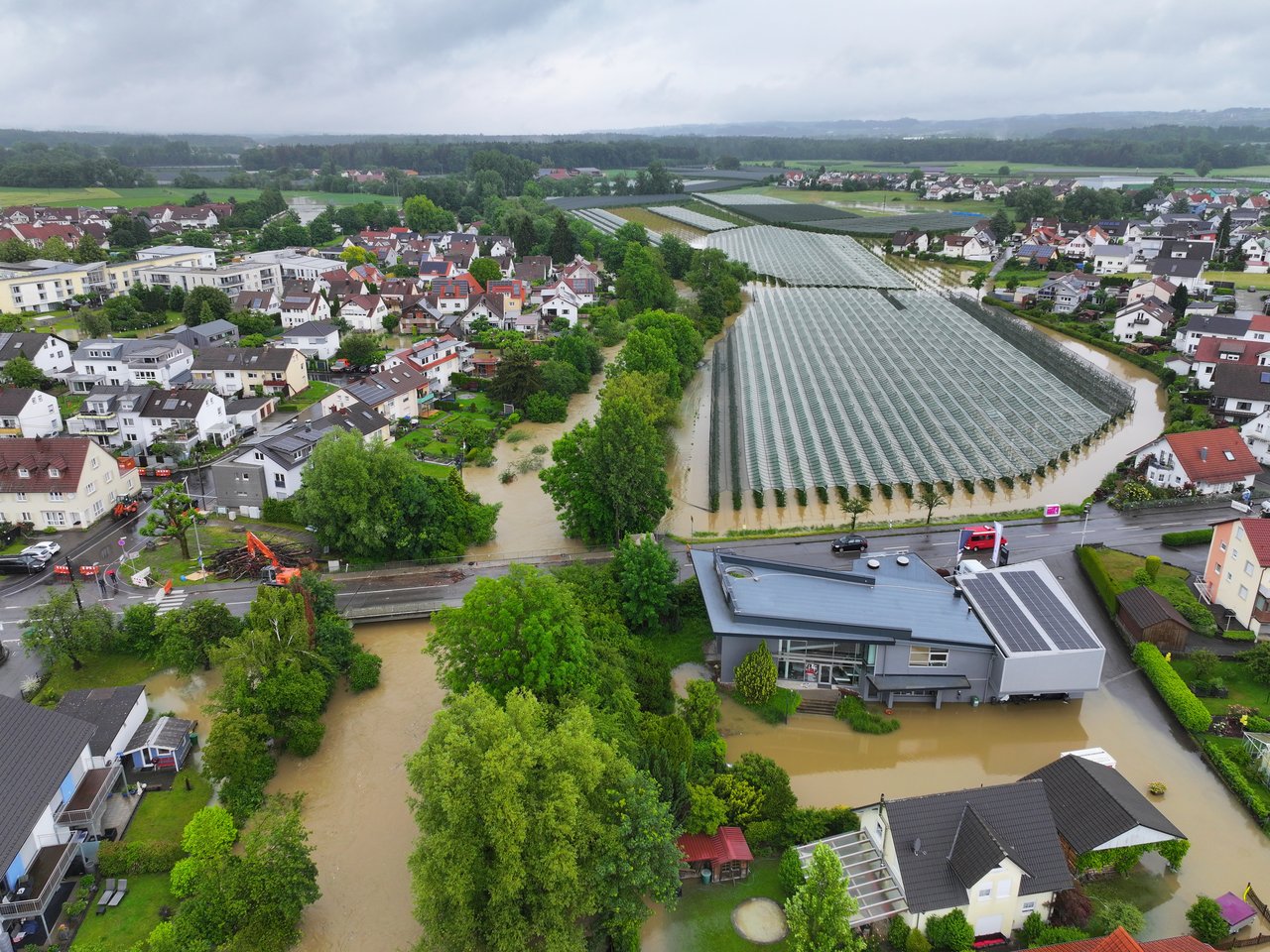 Das Foto zeigt eine Drohnenaufnahme von Brochenzell nach einem Hochwasserereignis. Man sieht die über das Ufer getretene Schussen und teilweise überschwemmtes Gelände