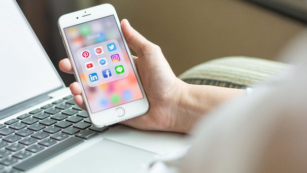 Eine Person sitzt im Sessel und schaut auf das Handy, auf dem sich social media icons sieht