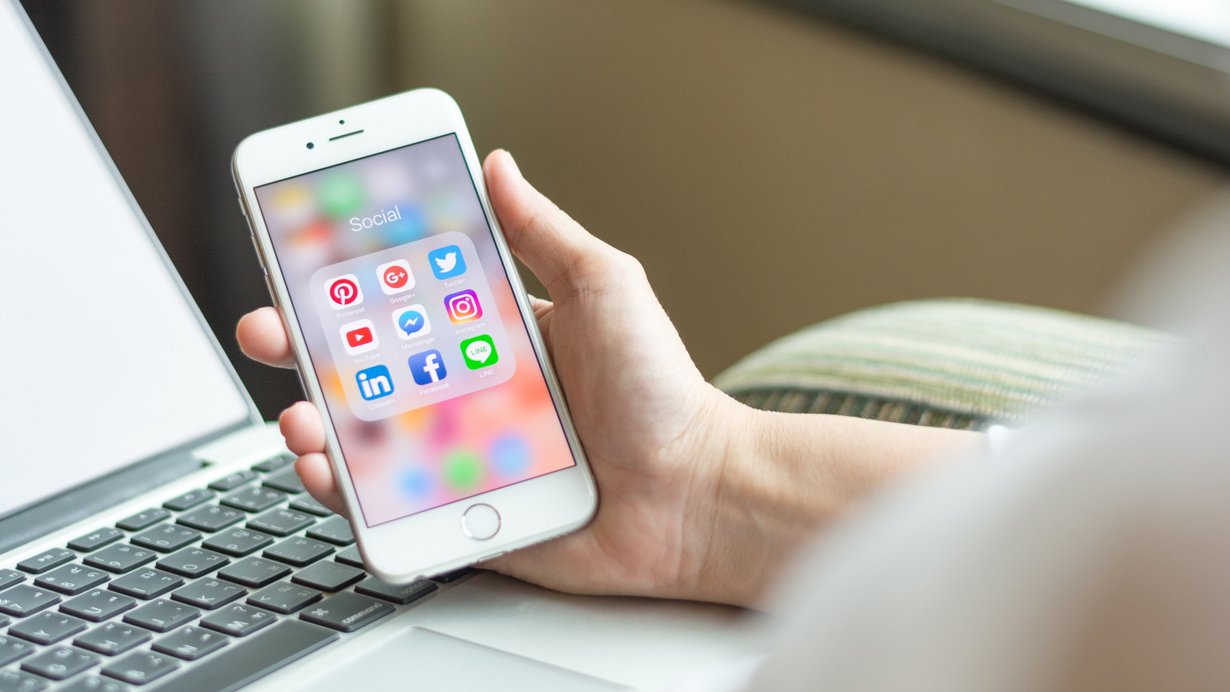 Eine Person sitzt im Sessel und schaut auf das Handy, auf dem sich social media icons sieht