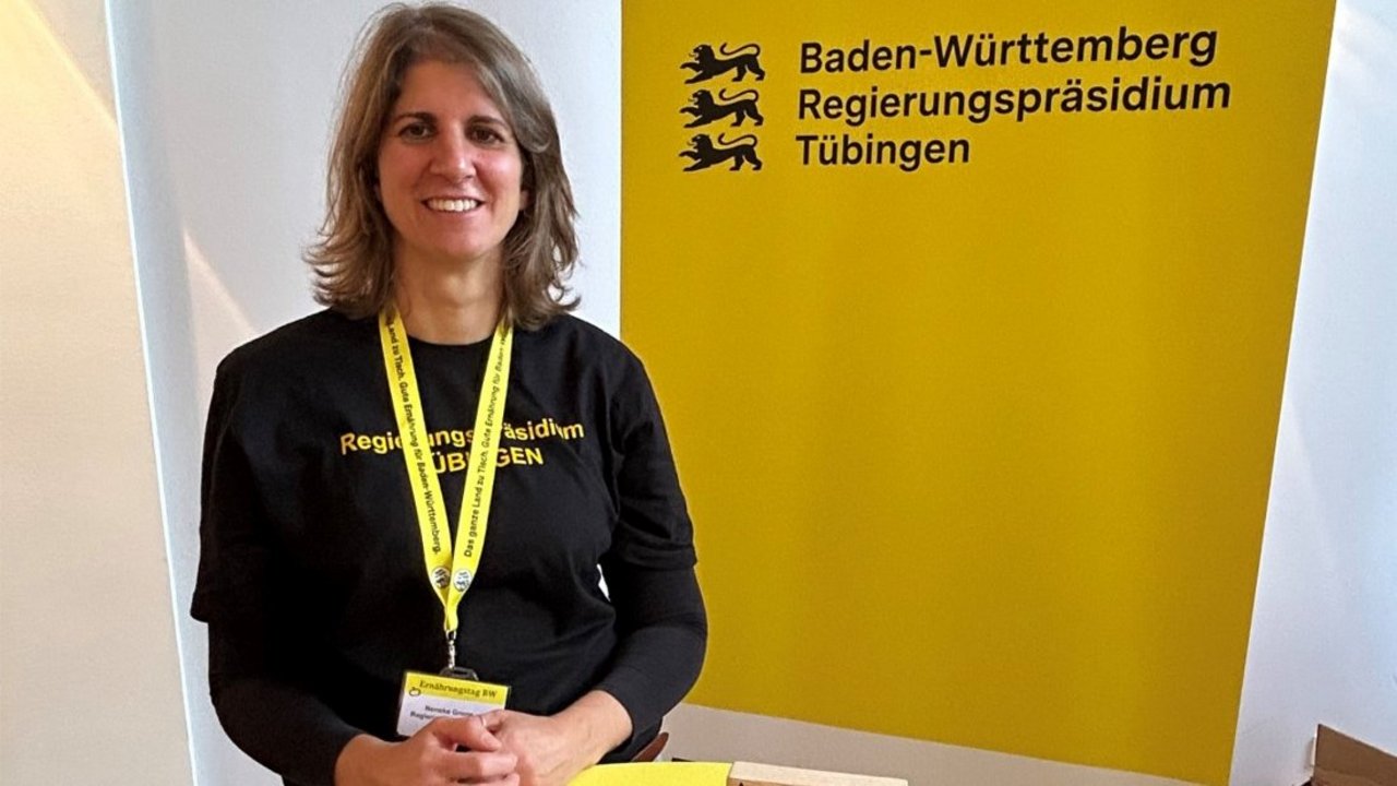 Eine Kollegin sthet hinter einem Tisch mit Materialien zu Berufen in der Hauswirtschaft und lächelt in die Kamera.