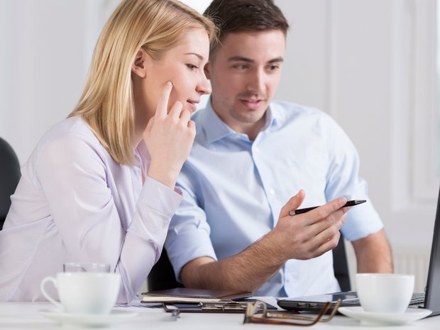 Junge Kollegen, eine Frau, ein Mann sitzen vor dem Laptop und diskutieren