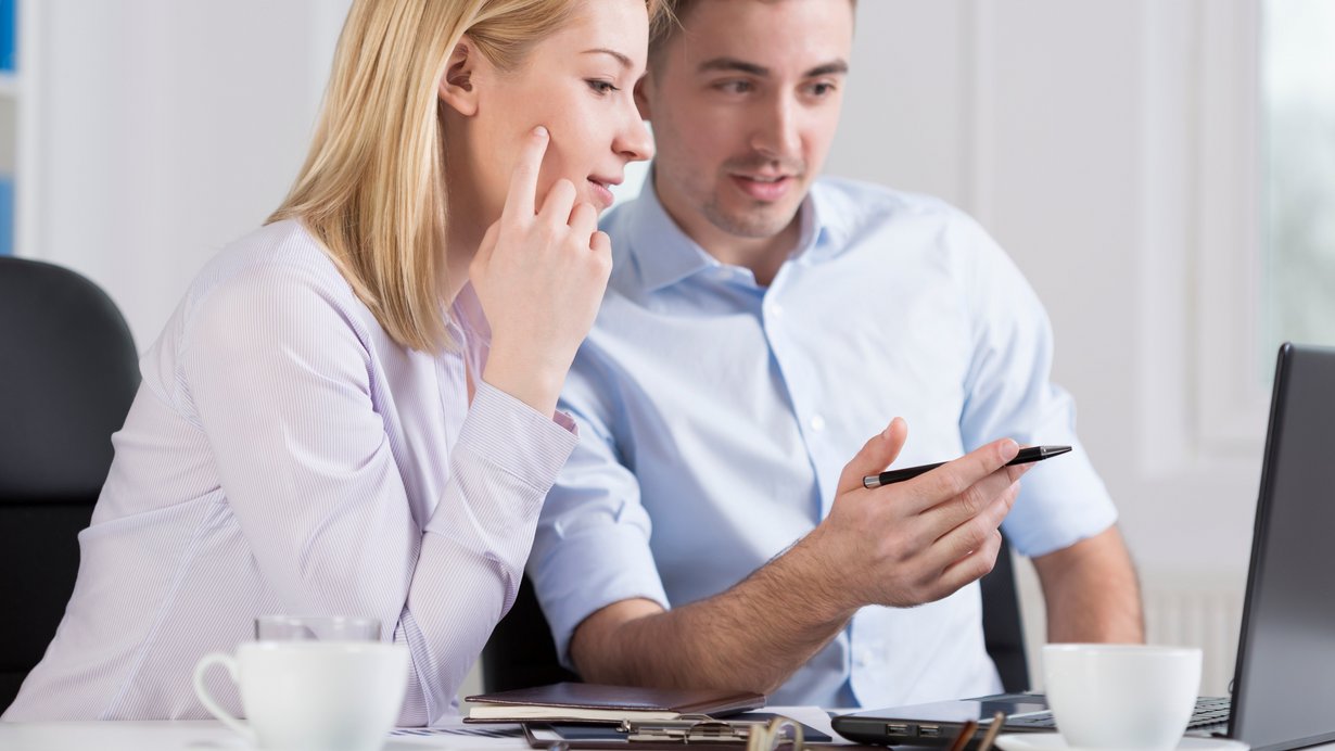 Junge Kollegen, eine Frau, ein Mann sitzen vor dem Laptop und diskutieren