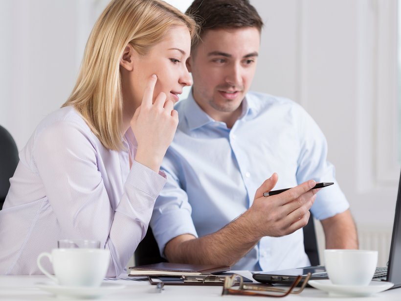 Junge Kollegen, eine Frau, ein Mann sitzen vor dem Laptop und diskutieren