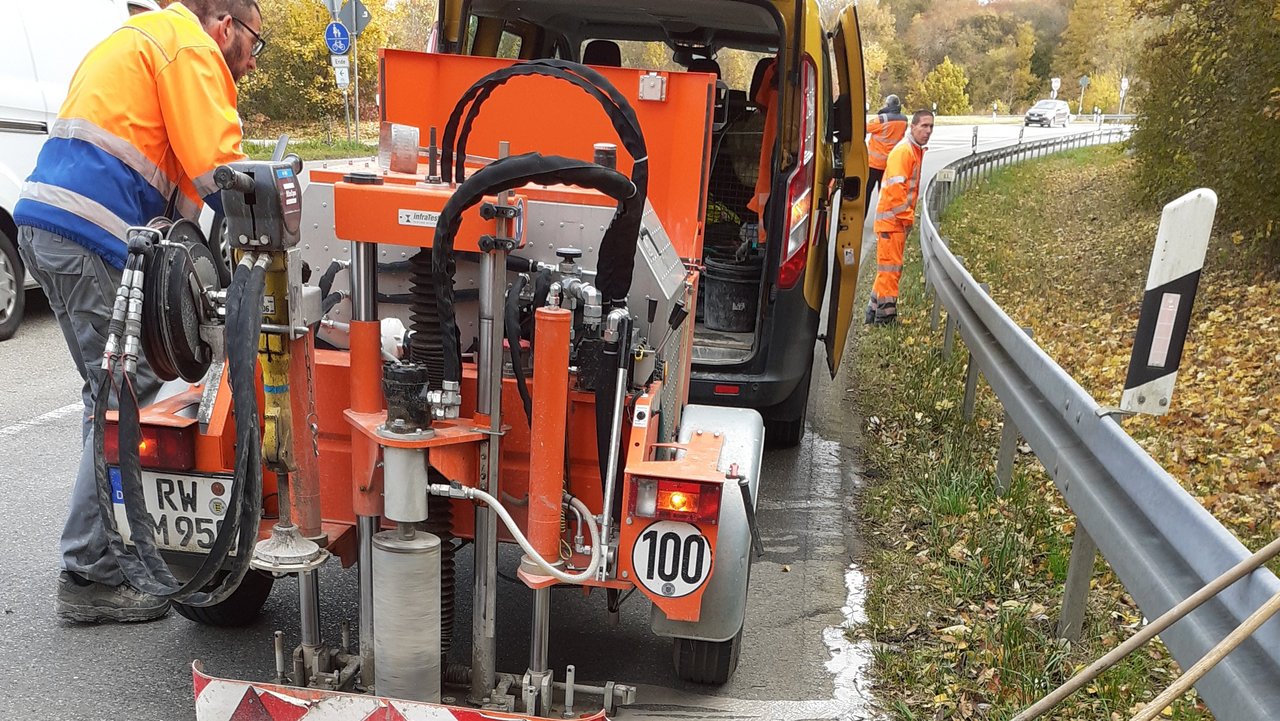 Ein Straßenbaumitarbeiter steht am Rand der Fahrbahn und bereitet ein Fahrzeug zur Bohrkernentnahme zur Material- und Zustandsuntersuchung vor.