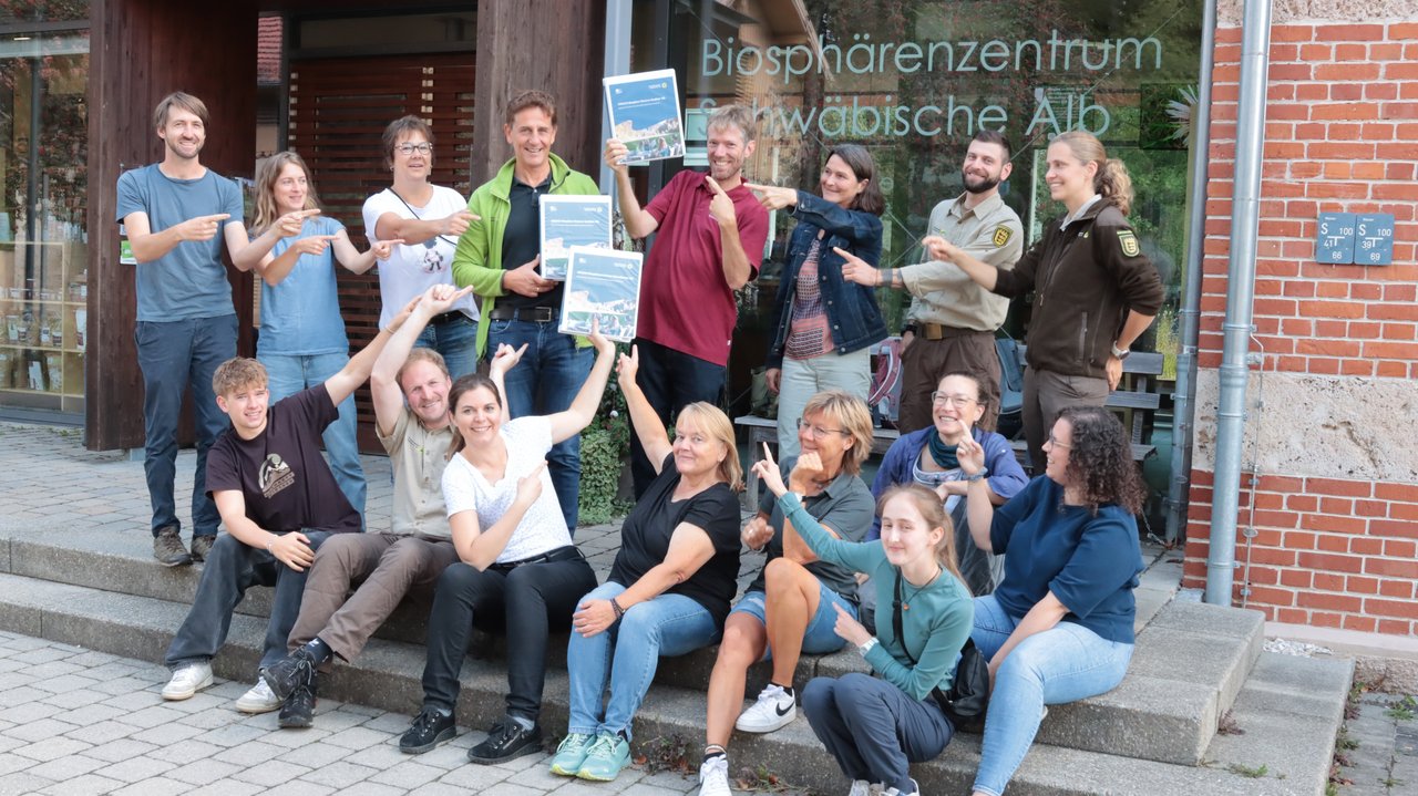 Das Foto zeigt ein Gruppenbild der Mitarbeitenden der Geschäftsstelle Biosphärengebeit Schwäbische Alb vor dem Biosphärenzentrum Schwäbische Alb. Drei Mitarbeitende halten den Antrag auf UNESCO-Anerkennung in der Hand.