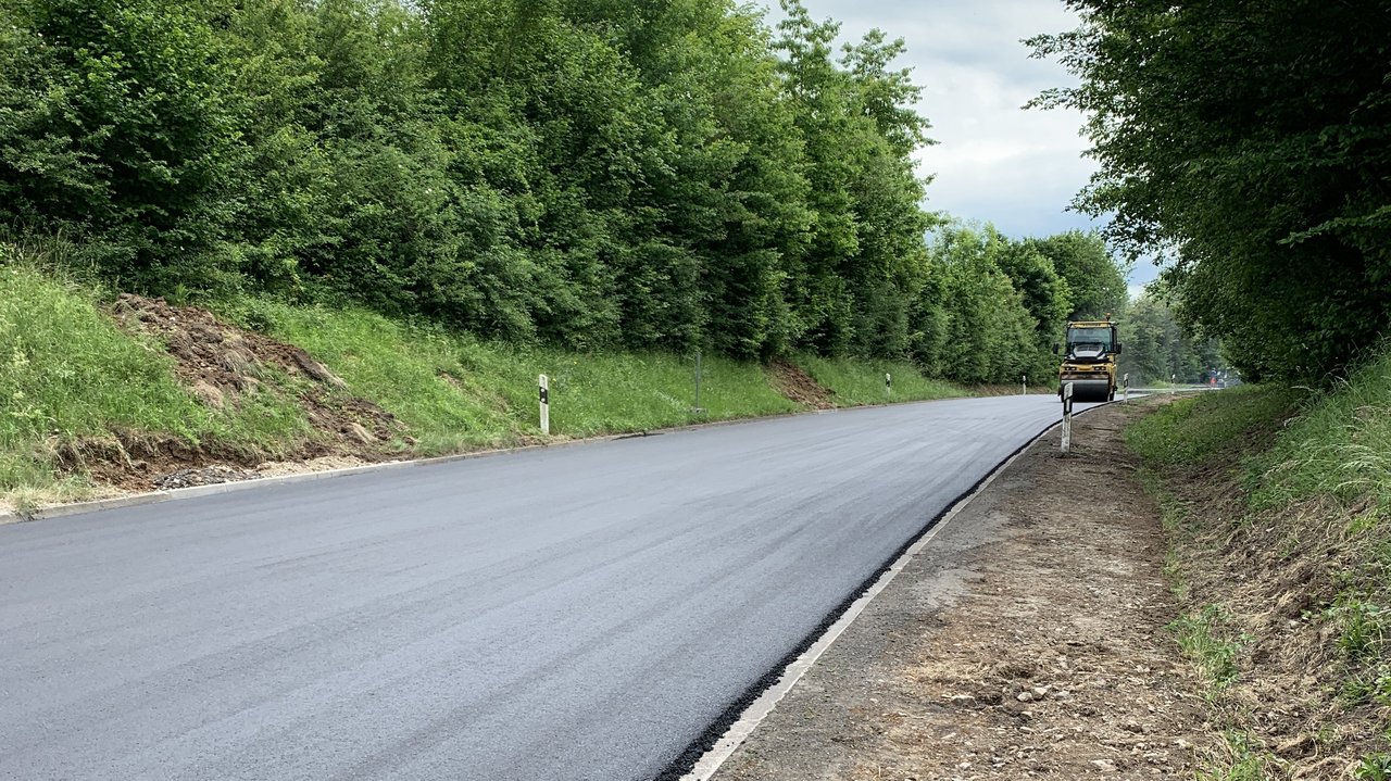 Das Foto zeigt eine frisch aspahltierte Straße und eine Straßenwalze