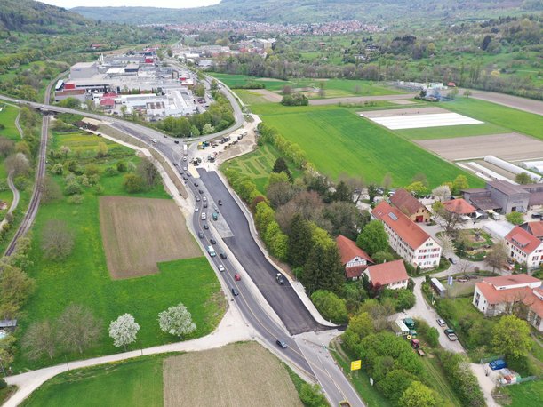 Luftbild einer Straßenbaustelle. Ein frisch asphaltierter Fahrstreifen schließt direkt an die bestehende Straße an und verbreitert diese. 