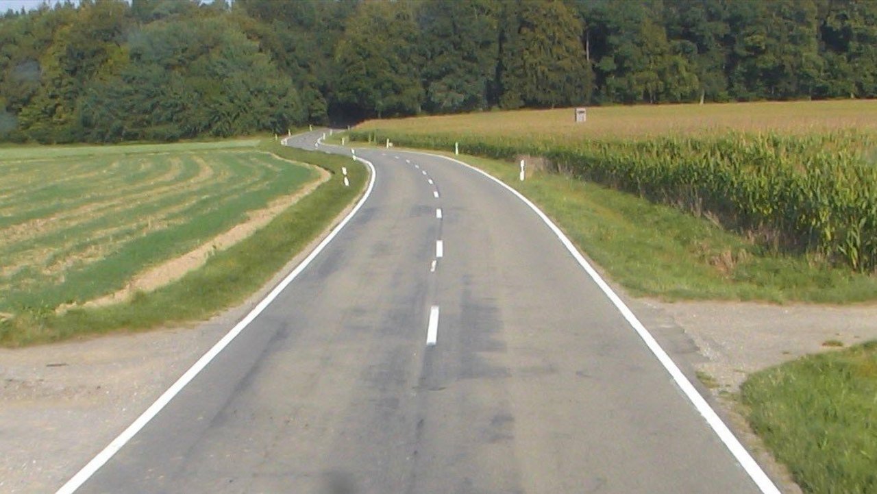 Das Foto zeigt die L 266 zwischen Attenweiler und Aßmannshardt; links und rechts Felder und Wiesen im Hintergrund Wald
