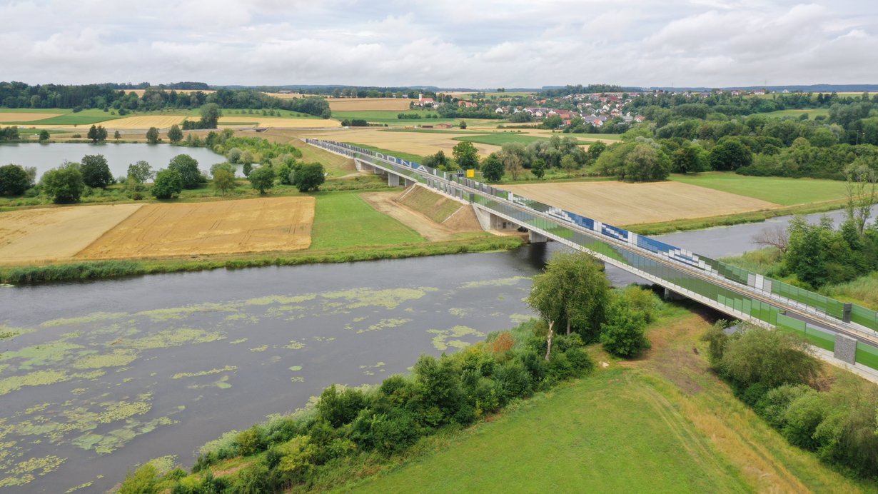 Luftbild von zwei Brücken über Gewässer. Auf den Irritationsschutzwänden stehen die Wörter "Donau" und "Kanal"Luftbild von zwei Brücken über Gewässer. Auf den Irritationsschutzwänden stehen die Wörter "Donau" und "Kanal"