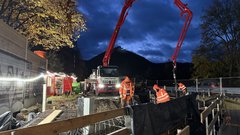 Ein LKW mit großem Ausleger steht an einer Baustelle. Der Ausleger reicht in eine Baugrube hinein. 