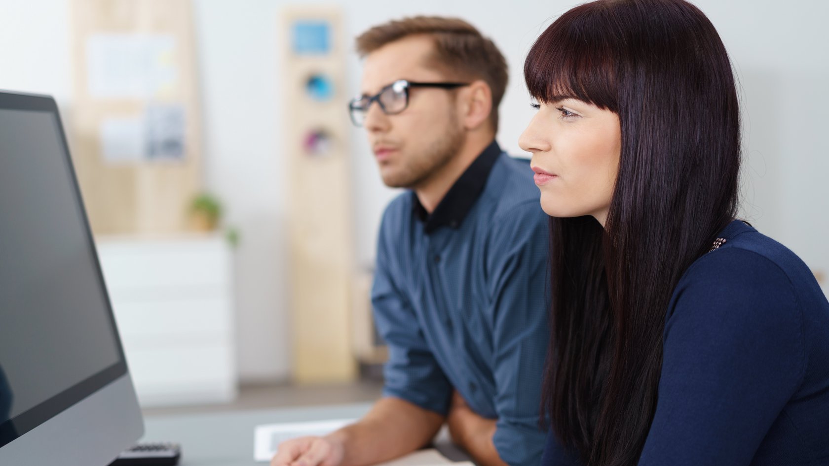 Eine Frau, ein Mann sitzen nachdenklich blickend am Computer