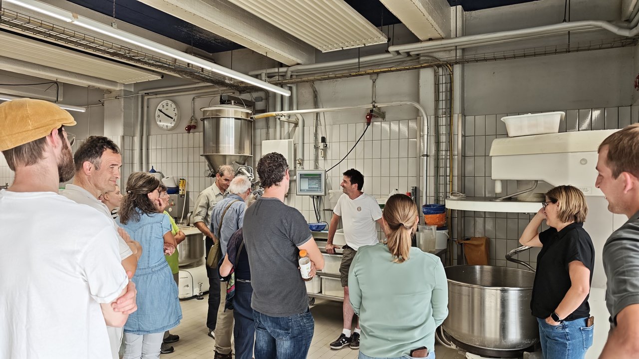 Das Foto zeigt mehrere Presonen in der Backstube der Bio-Bäckerei Berger. Man sieht große Rührmaschinen und weitere Backgeräte.